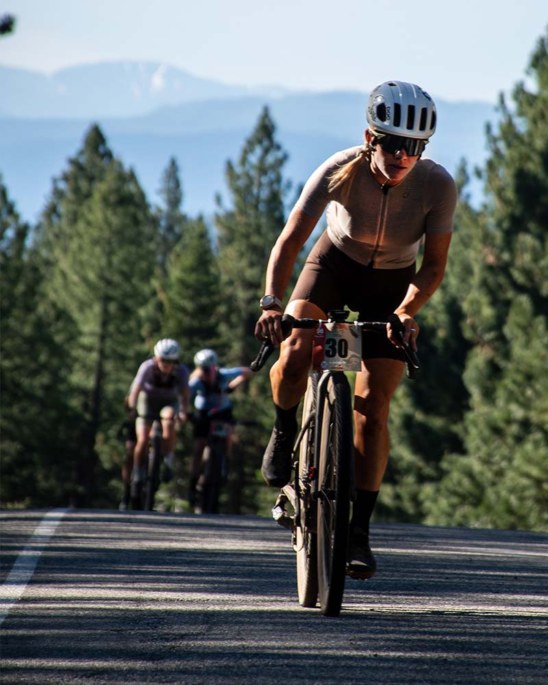 Woman gravel racer standing and pedaling hard on the top of a hill